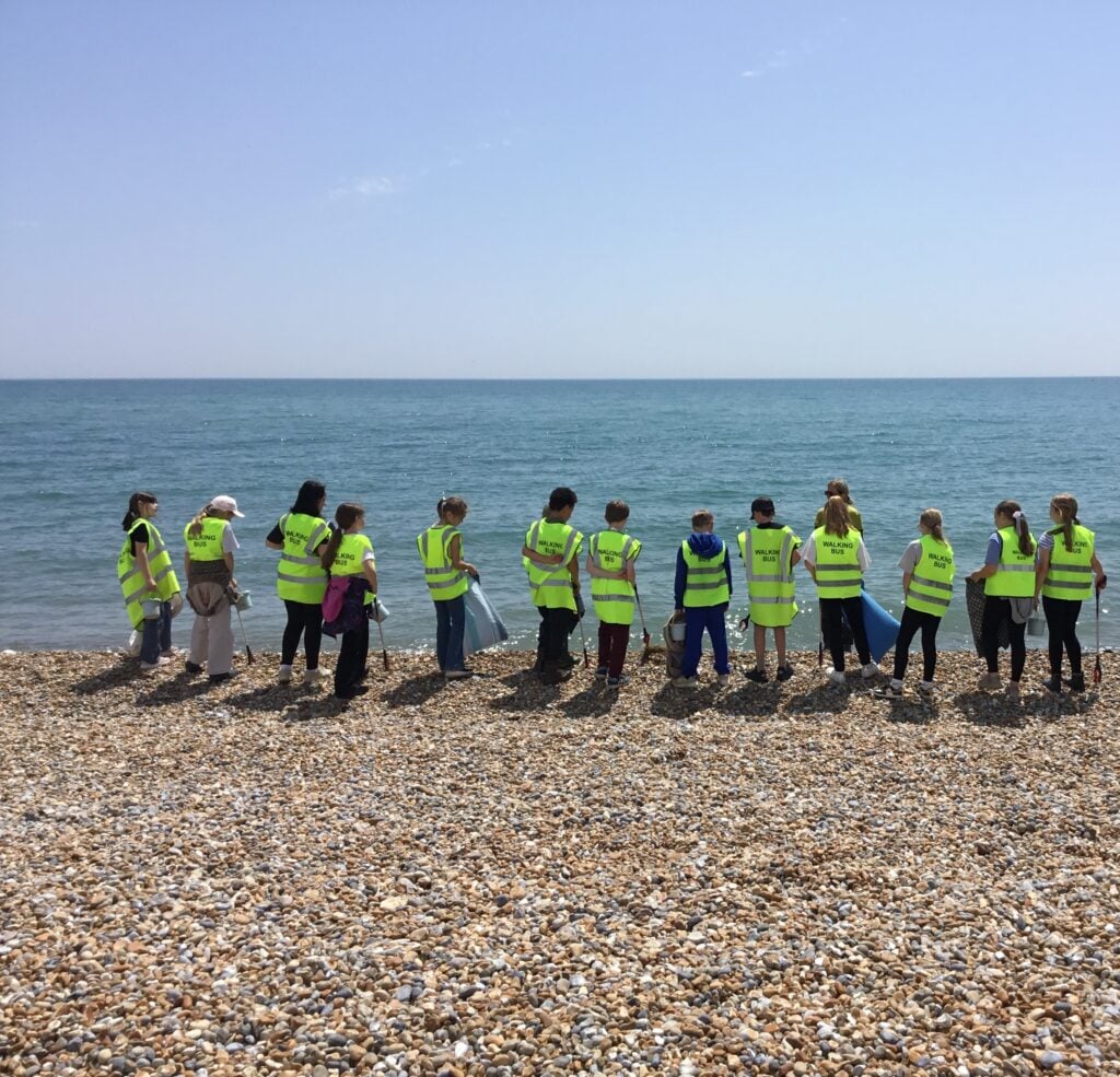 School children in hi-vis tabards lining up on pebbly beach with blue sea and sky in background