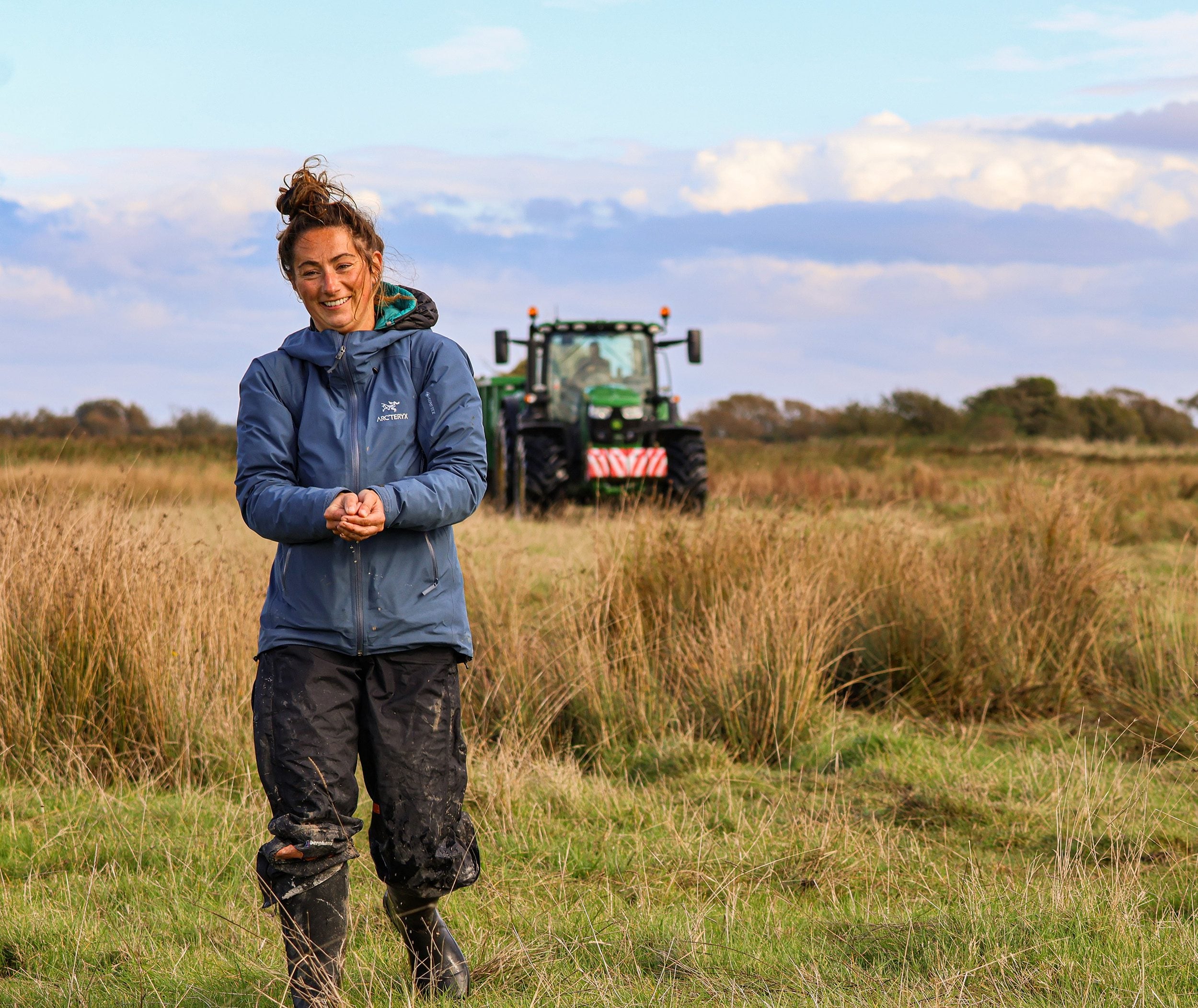 Person standing in field with long vegetation with tractor