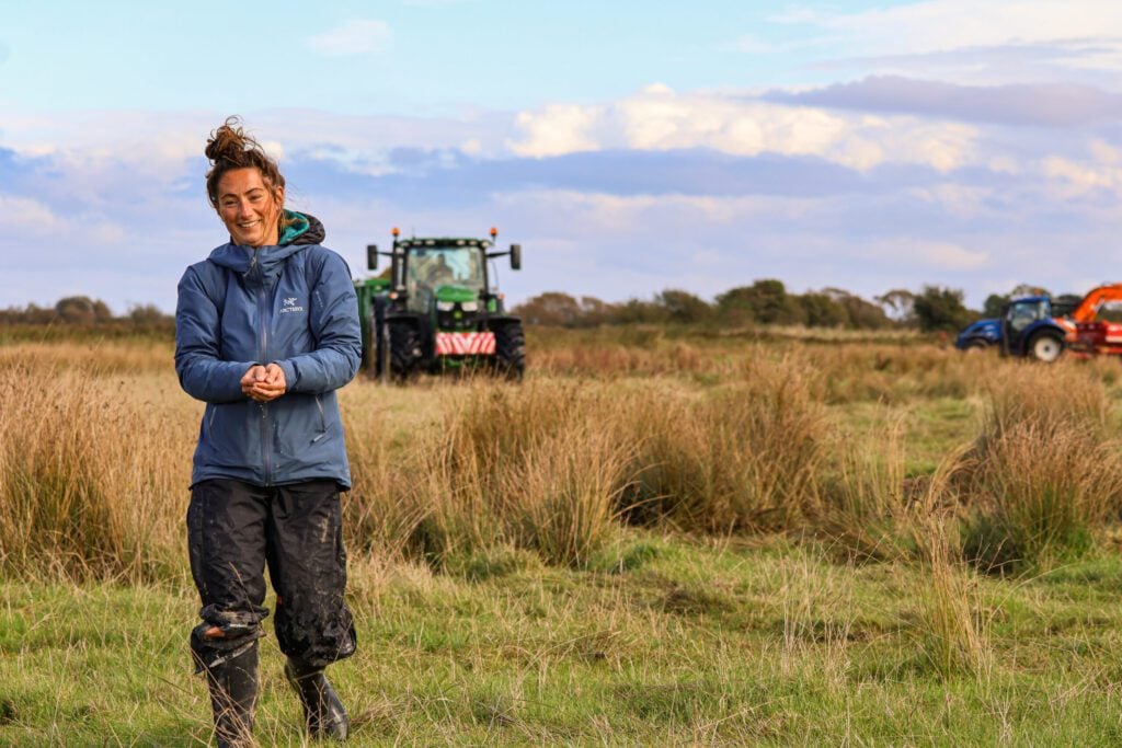 Person standing in field with long vegetation with tractor