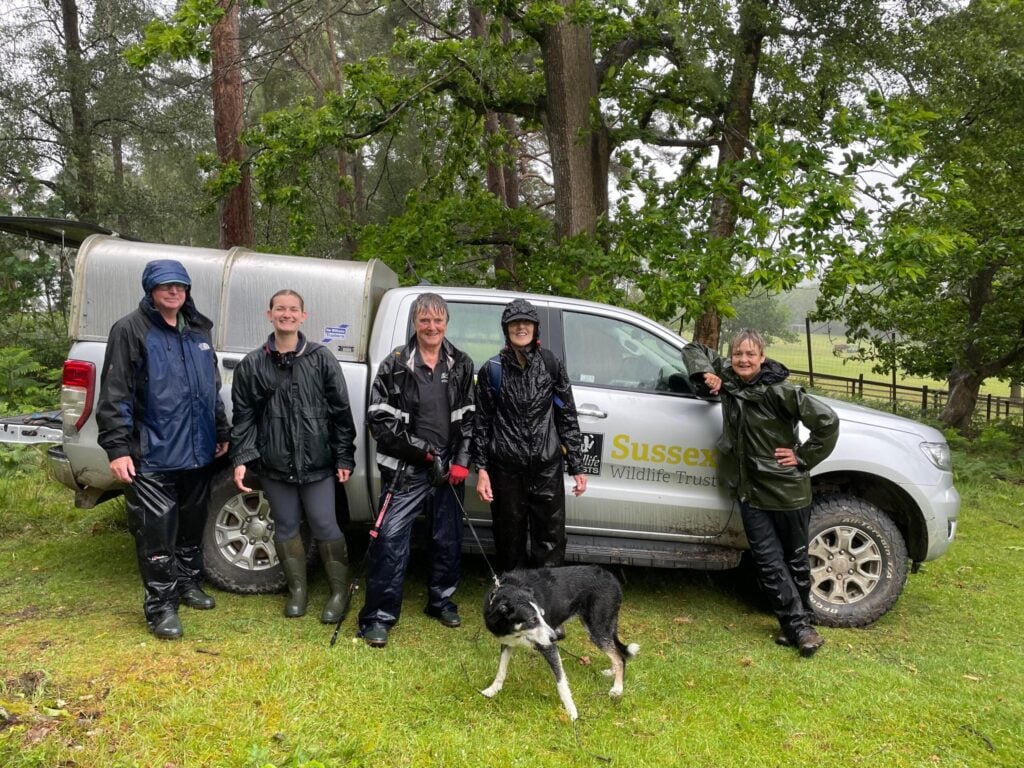 Five people and a dog standing beside 4-wheel drive truck in the rain