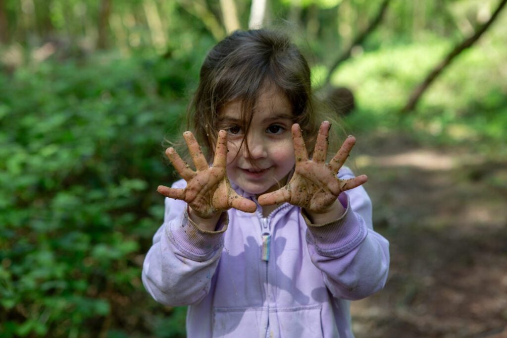 Child showing muddy hands to camera in woodland setting 
