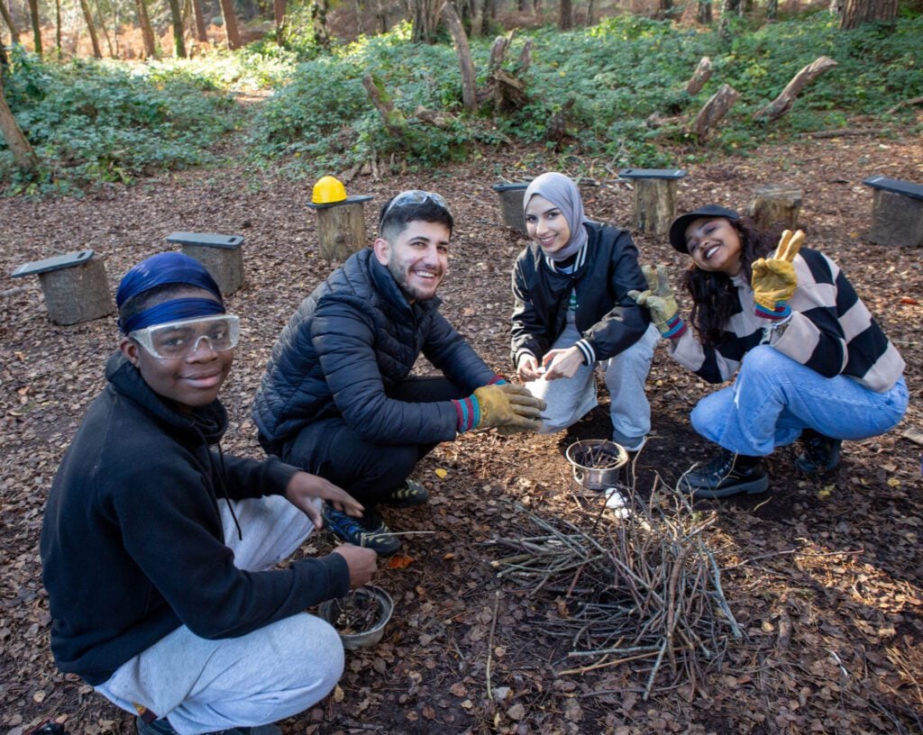 Four young people gathered on forest floor smiling at camera