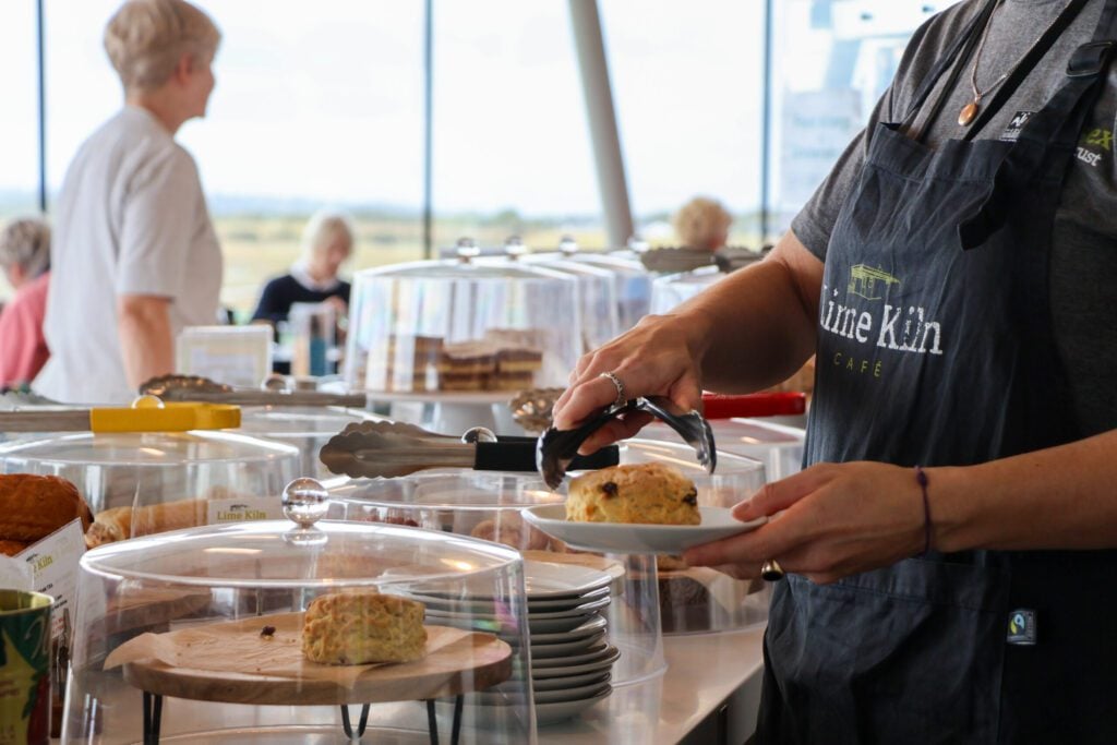Person at counter serving
 cake in cafe with customers in background