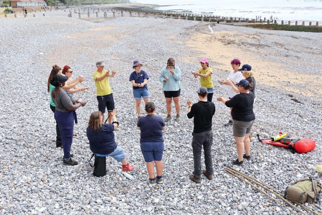 People standing in a circle on pebbly beach